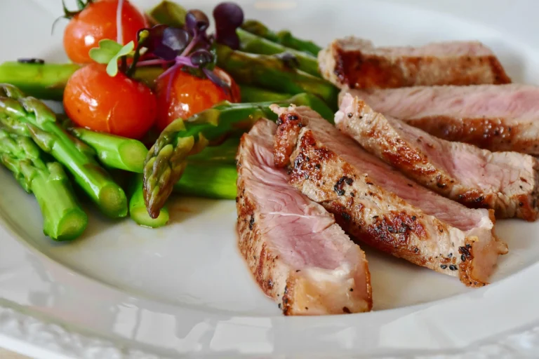 Sliced medium-rare Denver steak served with fresh asparagus and cherry tomatoes on a white plate